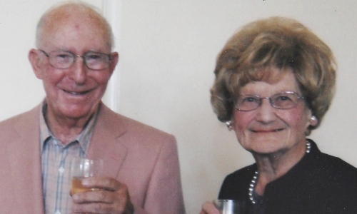 An older couple, both wearing glasses, smiling at the camera
