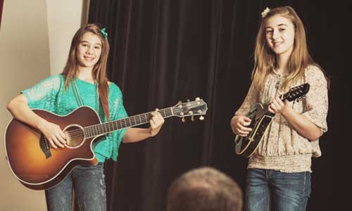 Two teenage girls play instruments as part of a talent show